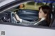 A woman sitting in a car with her hands on the steering wheel.