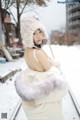 A woman in a white dress and hat standing in the snow.