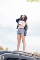 A woman standing on top of a car with her hands behind her head.