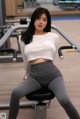 A woman in a white top and gray leggings sitting on a bench.