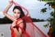 A woman in a red dress posing by the water.