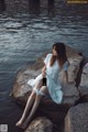 A woman sitting on a rock by the water.