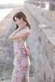 A woman in a pink floral dress leaning against a stone wall.