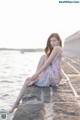 A woman sitting on a stone wall by the water.