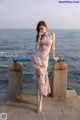 A woman in a pink dress standing on a pier by the ocean.