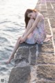 A woman sitting on a stone wall by the water.