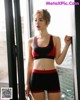 A woman in a red and black sports bra top and shorts.