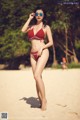 A woman in a red bikini standing on a beach.