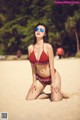 A woman in a red bikini sitting on a beach.