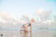 A woman in a bikini kneeling on the beach.