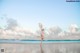 A woman in a blue bikini jumping in the air on a beach.