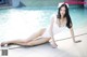 A woman in a white bathing suit sitting by a pool.