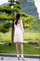 A woman in a white dress standing in front of a tree.