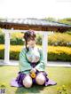 A woman in a kimono sitting on the grass with a flower in her hair.