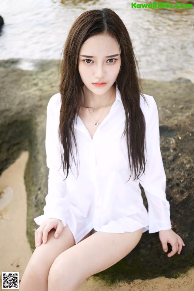 A woman sitting on a rock by the water.