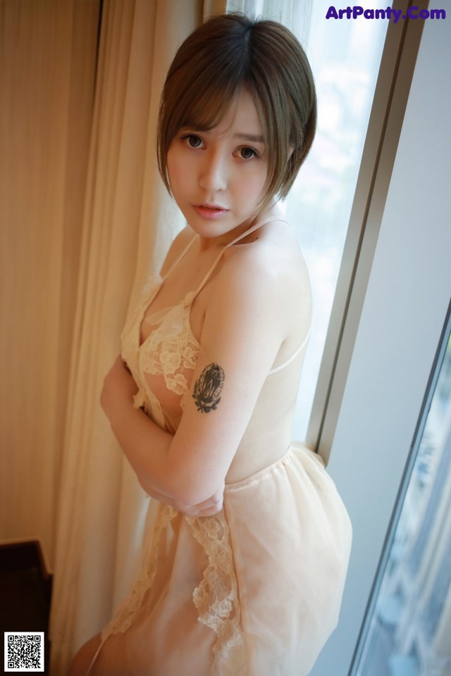 A woman with a tattoo on her arm standing by a window.
