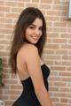 A woman in a black dress posing in front of a brick wall.