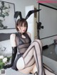 A woman in a black dress and bunny ears sitting on a bed.