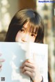 A young woman holding a book in front of her face.