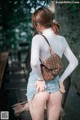 A woman in a white shirt and denim shorts holding a brown bag.