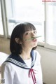 A woman in a sailor outfit holding a pencil in her mouth.