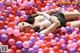 A woman laying in a ball pit of pink and purple balls.