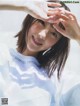 A woman in a white shirt holding her hands up to her face.