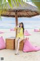 A woman in a yellow dress sitting on a wooden bench on the beach.