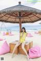 A woman in a yellow bathing suit sitting on a wooden bench on the beach.