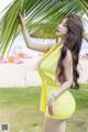 A woman in a yellow dress posing under a palm tree.