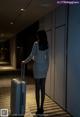 A woman in a business suit with a suitcase in a hallway.