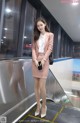 A woman in a pink suit standing on an escalator.